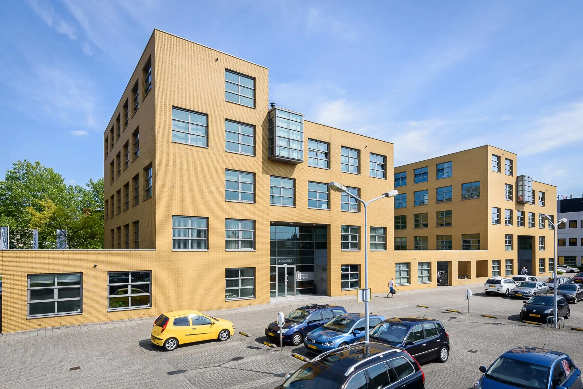 Kantoorgebouw aan de Rivium 2e Straat met geparkeerde auto's op de voorgrond op een zonnige dag.